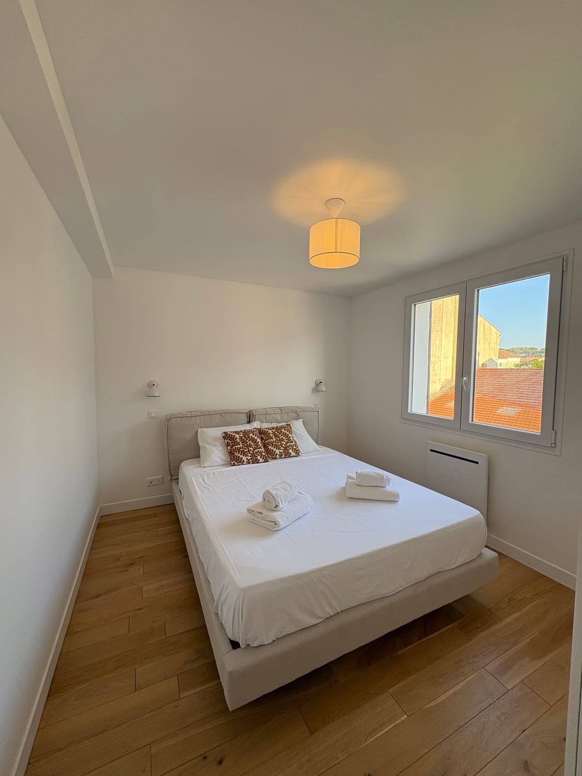 Chambre en lin blanc, réveillée par un coussin aux tons chauds — Sanary-sur-Mer — deux appartements meublés